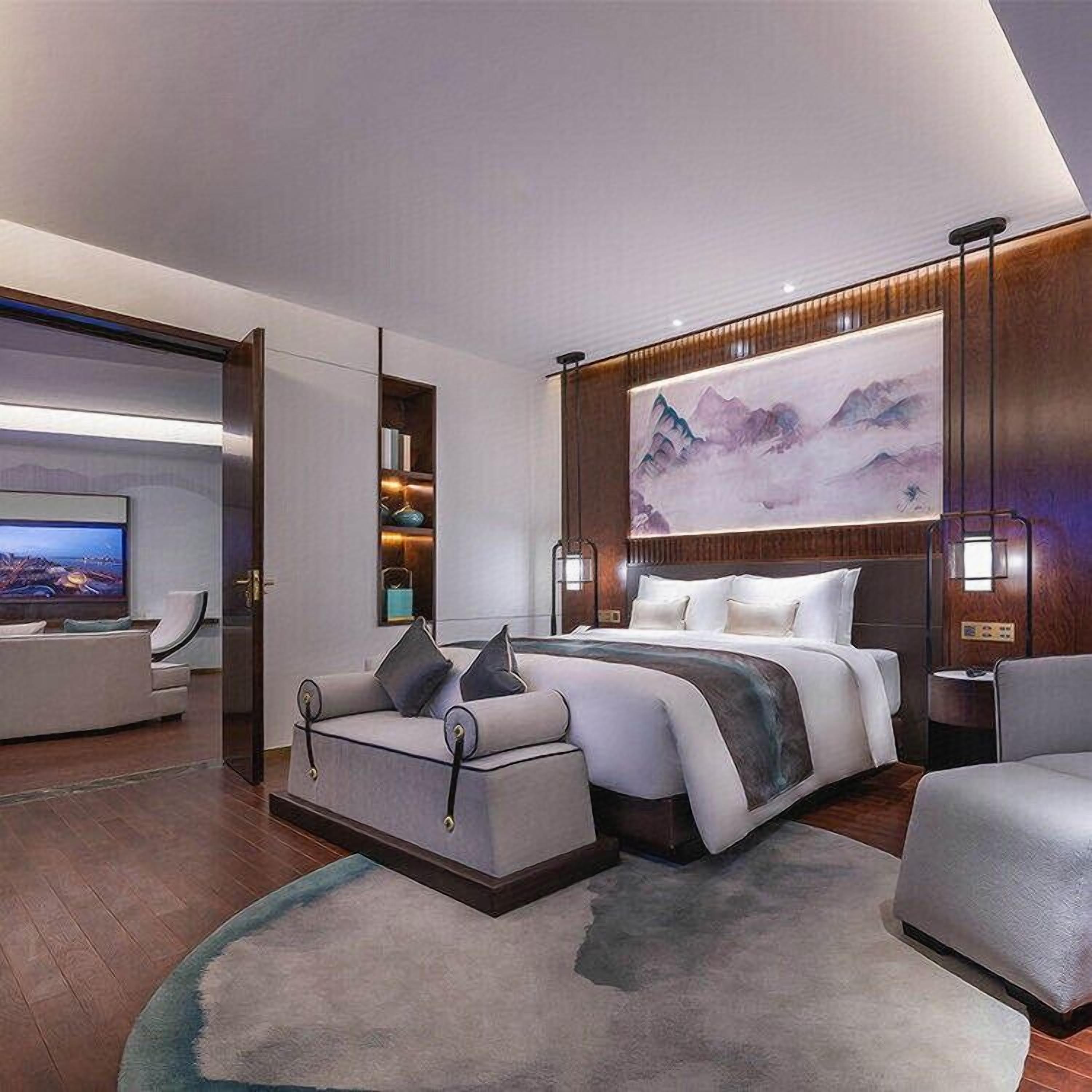 A modern hotel room with a large bed, a sofa, a TV, and a painting on the wall.