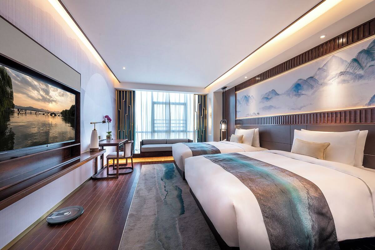A modern hotel room with a large bed, a desk, and a television displaying a scenic view.