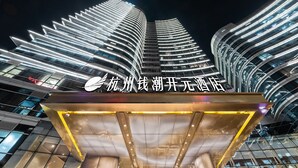A modern hotel entrance with a distinctive curved facade and illuminated signage. - Hangzhou Binjiang Qianchao New Century Hotel (Hangzhou)