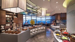 A modern hotel lobby with a central buffet area, large windows, and a view of the cityscape. - Hangzhou Binjiang Qianchao New Century Hotel (Hangzhou)