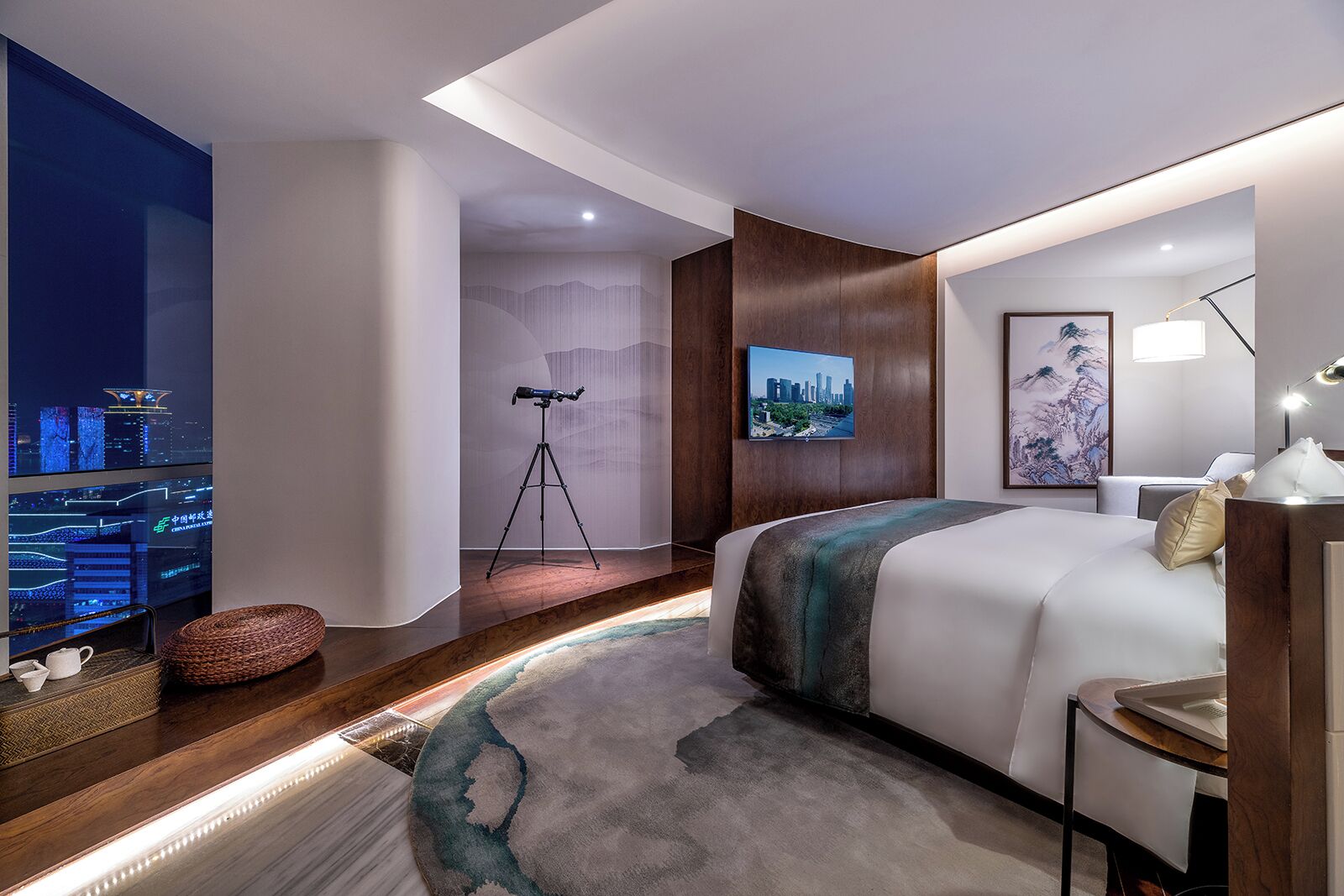 Una habitación de hotel moderna con una cama grande, un escritorio, una lámpara de escritorio, un telescopio, una vista de la ciudad en la pared y una vista nocturna en la televisión.