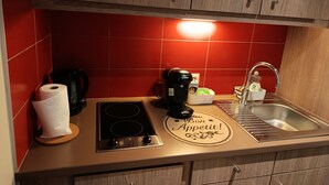 Une cuisine avec des carreaux rouges, une machine à café Bosch, une bouilloire, un évier et un plan de travail orné d’une pancarte indiquant « Bon appétit ! ».
