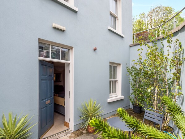 Una casa azul con la puerta abierta, una ventana pequeña y un banco.