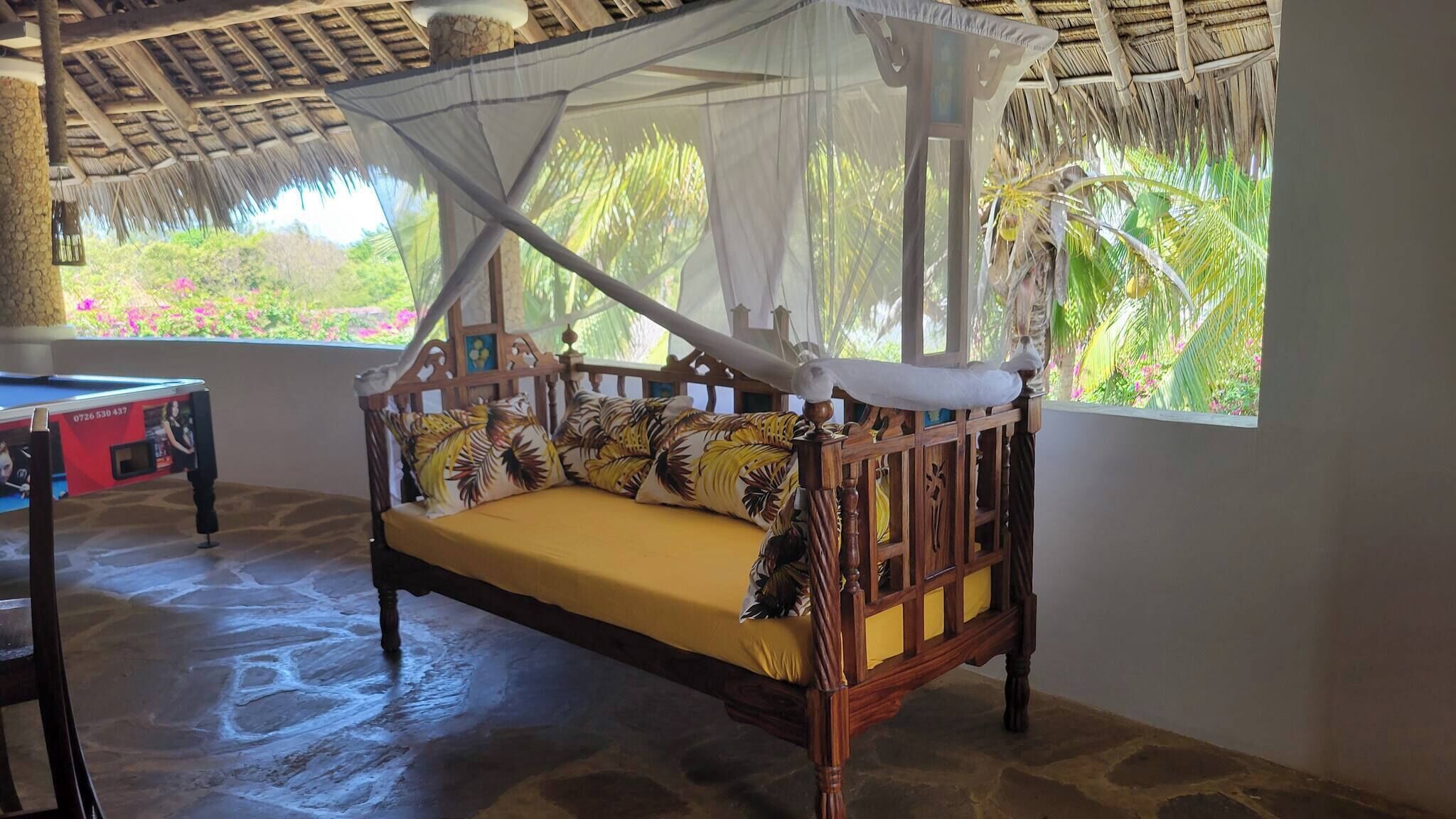 A wooden bed with a canopy, a small table with a TV, and a view of greenery outside.