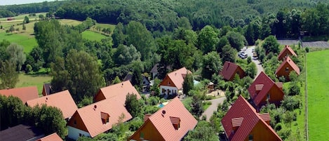 En samling rödmålade stugor omgivna av gröna fält och träd, med en klar himmel ovanför.