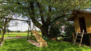A wooden play structure with a slide and swings, a tree, and a small shed. - Gemütliches Ferienwohnung in Feldwies mit Sauna (Ubersee)