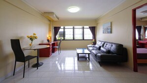 A living room with a sofa, a dining table, and chairs. There is a window with curtains, a painting on the wall, and a vase with flowers on the table. - Petch Tower Ekkamai (Bangkok)