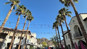 A pedestrian street lined with palm trees and buildings, featuring outdoor seating areas and string lights. - Sun-Soaked Condo near Old Town (La Quinta)