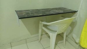 Une petite pièce avec une chaise en plastique blanc et une table à plateau en marbre noir, le tout adossé à un mur uni.