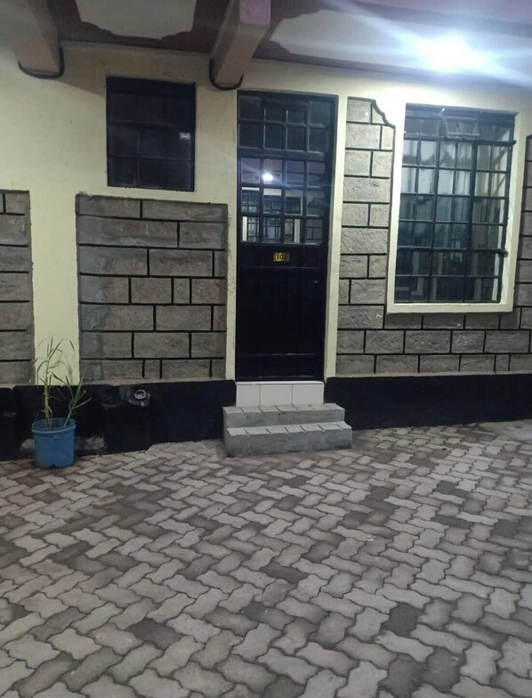 Un edificio con fachada de ladrillo, una puerta negra con una placa de número y una planta en maceta.