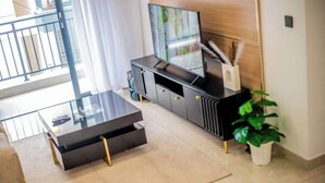 A modern living room with a glass coffee table, a flat-screen TV on a black entertainment unit, and a potted plant. - New Dawn Home (Nairobi)