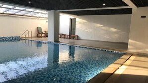 An indoor swimming pool with a tiled floor, a sunlit ceiling, and a few lounge chairs. - New Dawn Home (Nairobi)