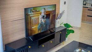 A modern living room with a flat-screen TV mounted on a black entertainment unit, a coffee table with a glass top, and a potted plant. - New Dawn Home (Nairobi)