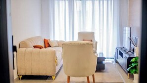 A modern living room with a beige sofa, a white armchair, and a black entertainment unit. - New Dawn Home (Nairobi)