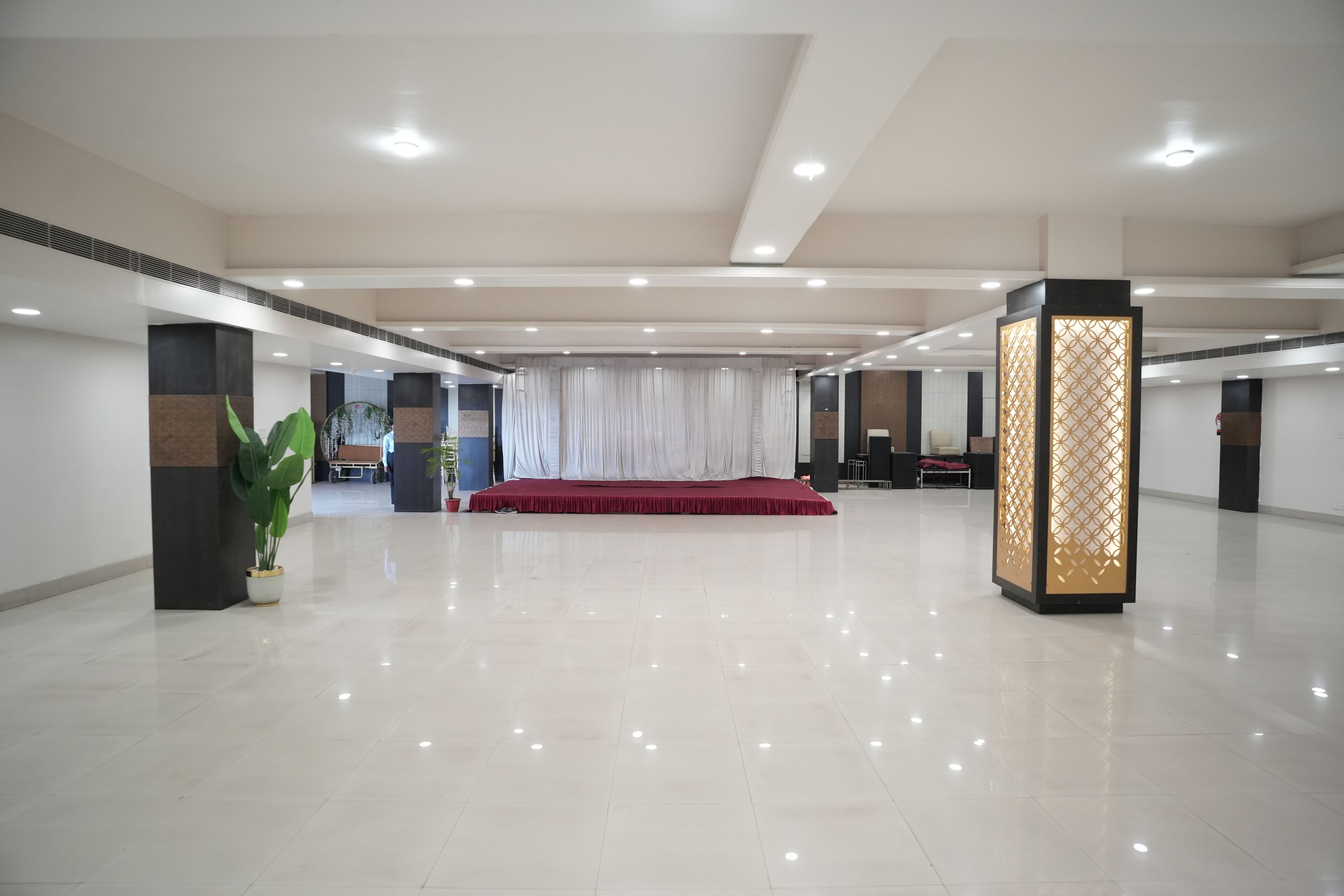 A spacious hotel lobby with a red carpet, potted plants, and a decorative screen.
