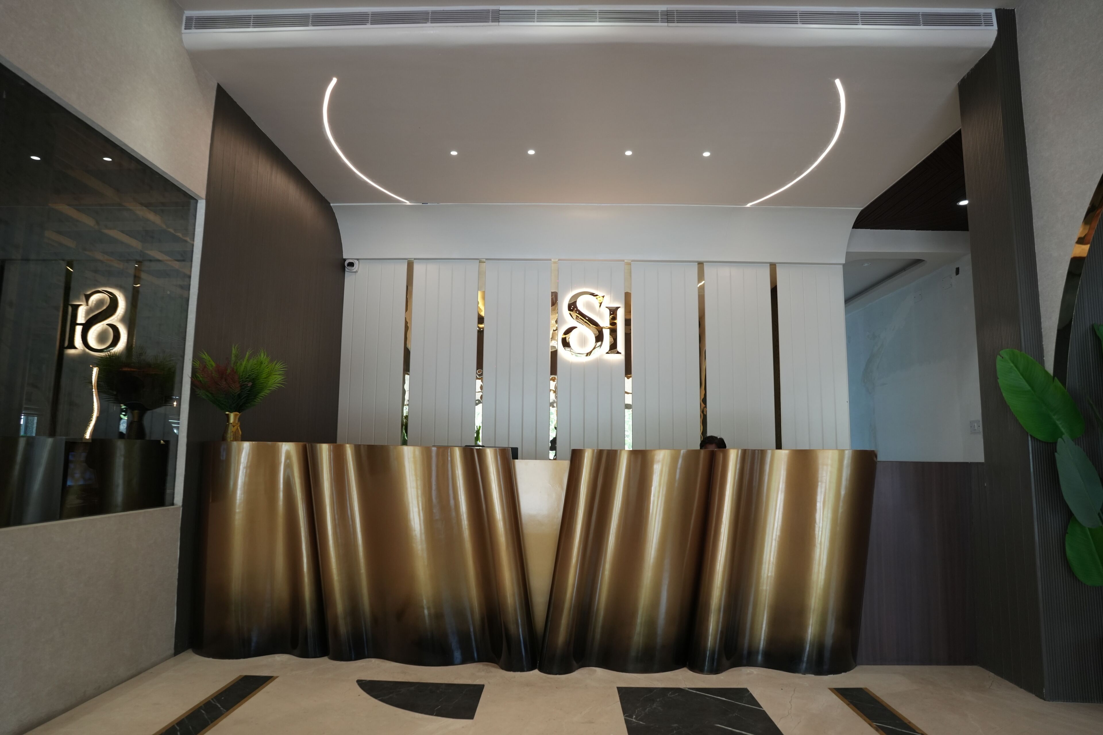 A reception area with a modern design, featuring a reception desk, a large mirror, and a plant.
