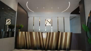 Un área de recepción con diseño moderno, que incluye un mostrador de recepción, un espejo grande y una planta.
