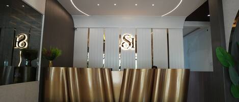 A reception area with a modern design, featuring a reception desk, a large mirror, and a plant.