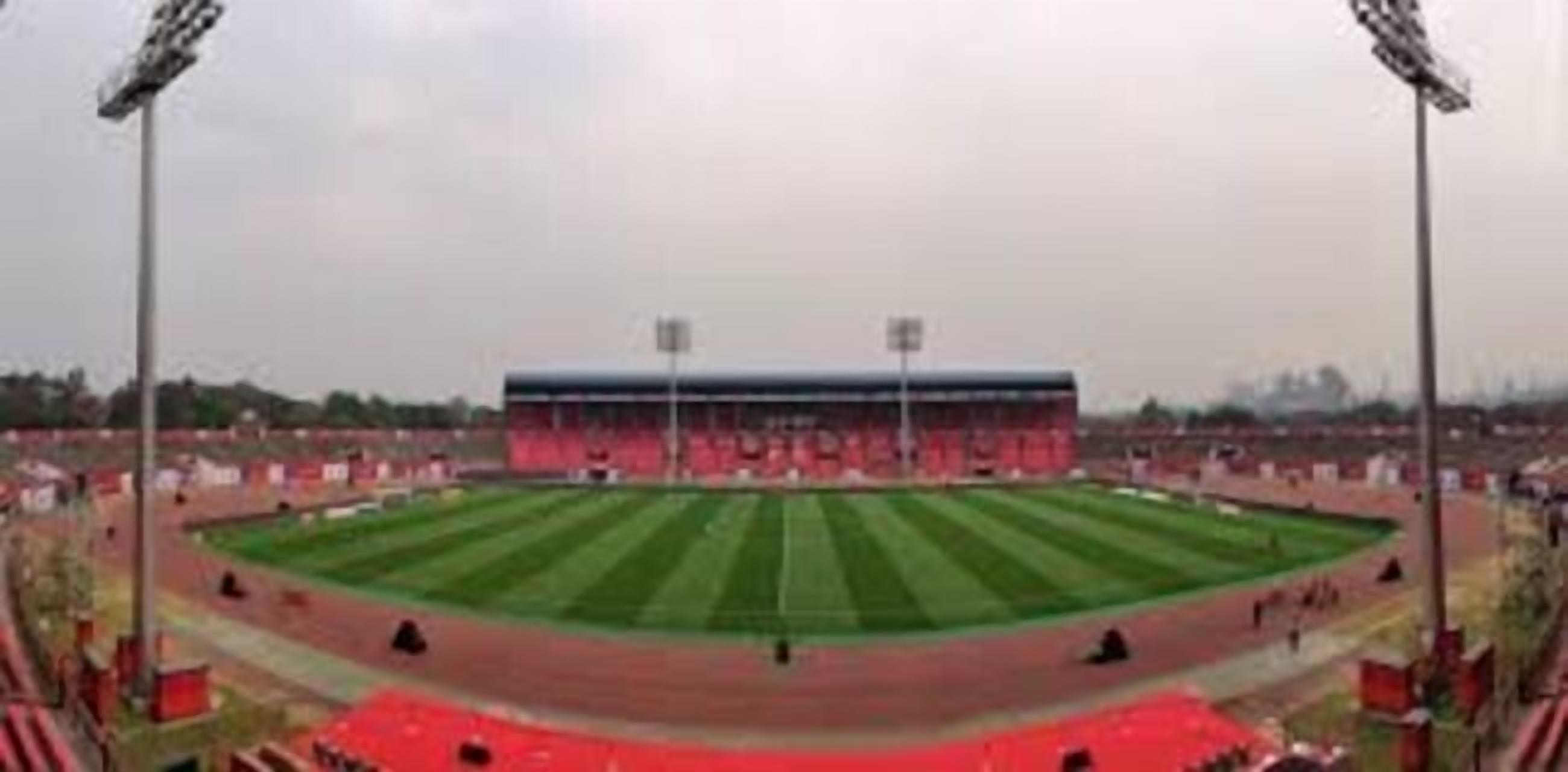 Un estadio con campo central, gradas para espectadores y focos.