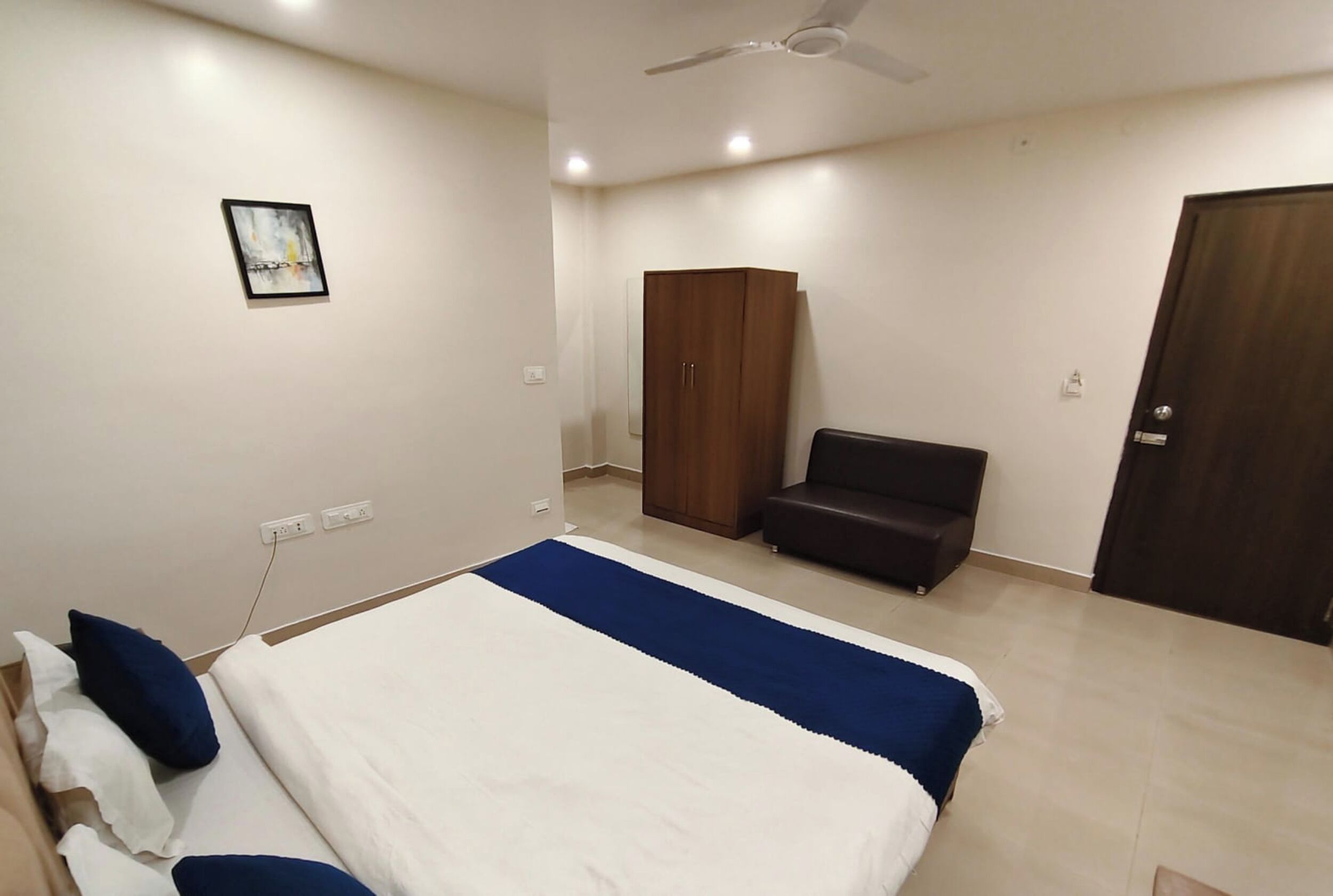 A bedroom with a bed, a wardrobe, a sofa, and a ceiling fan.
