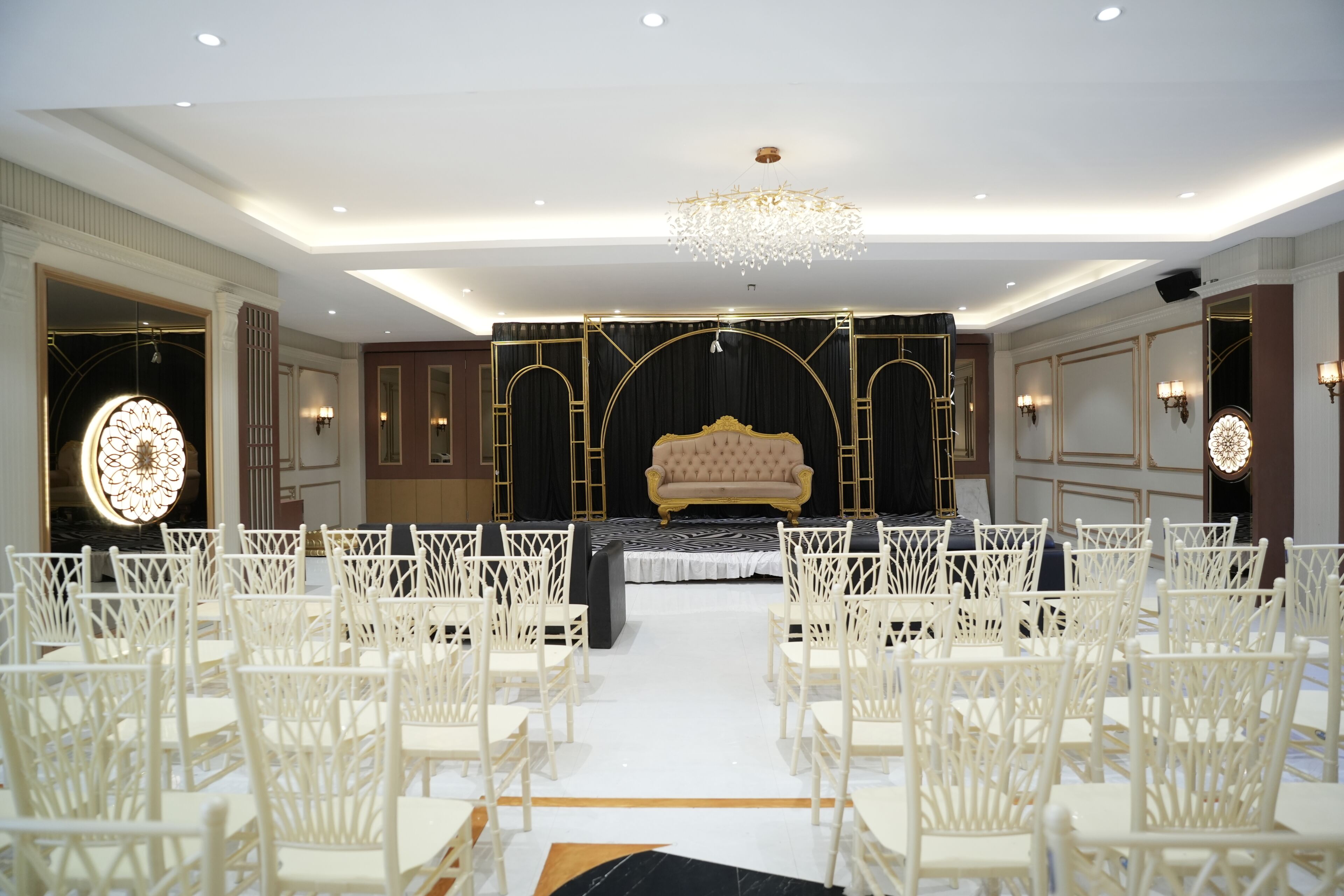 A formal event space with a stage, white chairs, and a chandelier.