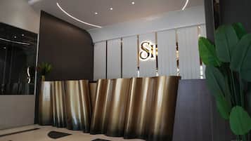 Zona de recepción con diseño moderno, que incluye un mostrador metálico y un gran letrero iluminado con la letra 'S'.