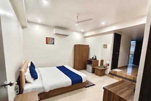 Una habitación de hotel moderna con cama, armario, escritorio y un refrigerador pequeño.