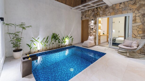 An indoor swimming pool with tiled flooring, a stone wall, and a wooden ceiling. - Casa De Vero Amore 3 (Jimbaran)