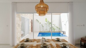 A dining area with a table set for four, overlooking a swimming pool and greenery. - Casa De Vero Amore 3 (Jimbaran)