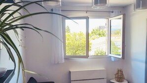 Moderni olohuone, jossa on sohva, pieni pöytä ja ikkuna, josta avautuu näkymä vehreään maisemaan.