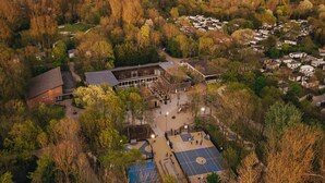 Vista aérea de una zona residencial con un edificio grande, canchas de baloncesto y árboles circundantes.