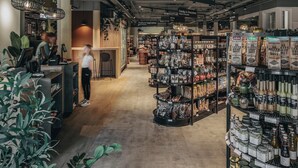 Interior de una tienda con estanterías llenas de diversos productos, una caja registradora y una sección que dice 'Baby & Souvenirs'.