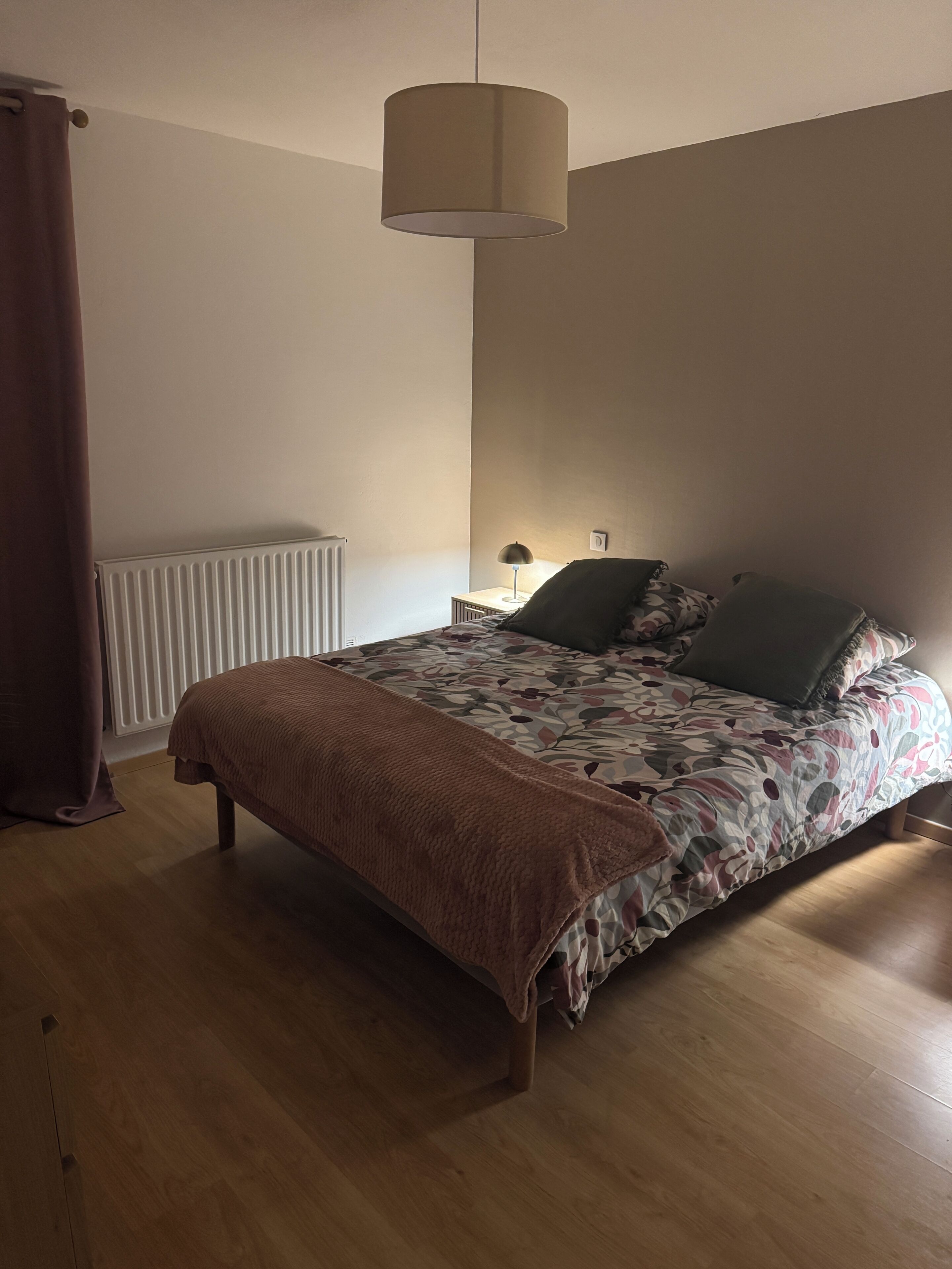 A bedroom with a bed, a radiator, a lamp, and a hanging light fixture.