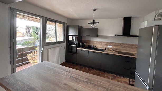 Cocina compacta con encimera de madera, electrodomésticos integrados y vistas a través de la puerta de cristal.