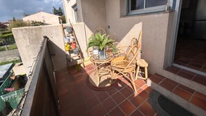 Un pequeño patio al aire libre con una mesa redonda y sillas de mimbre, una planta en maceta y un taburete.