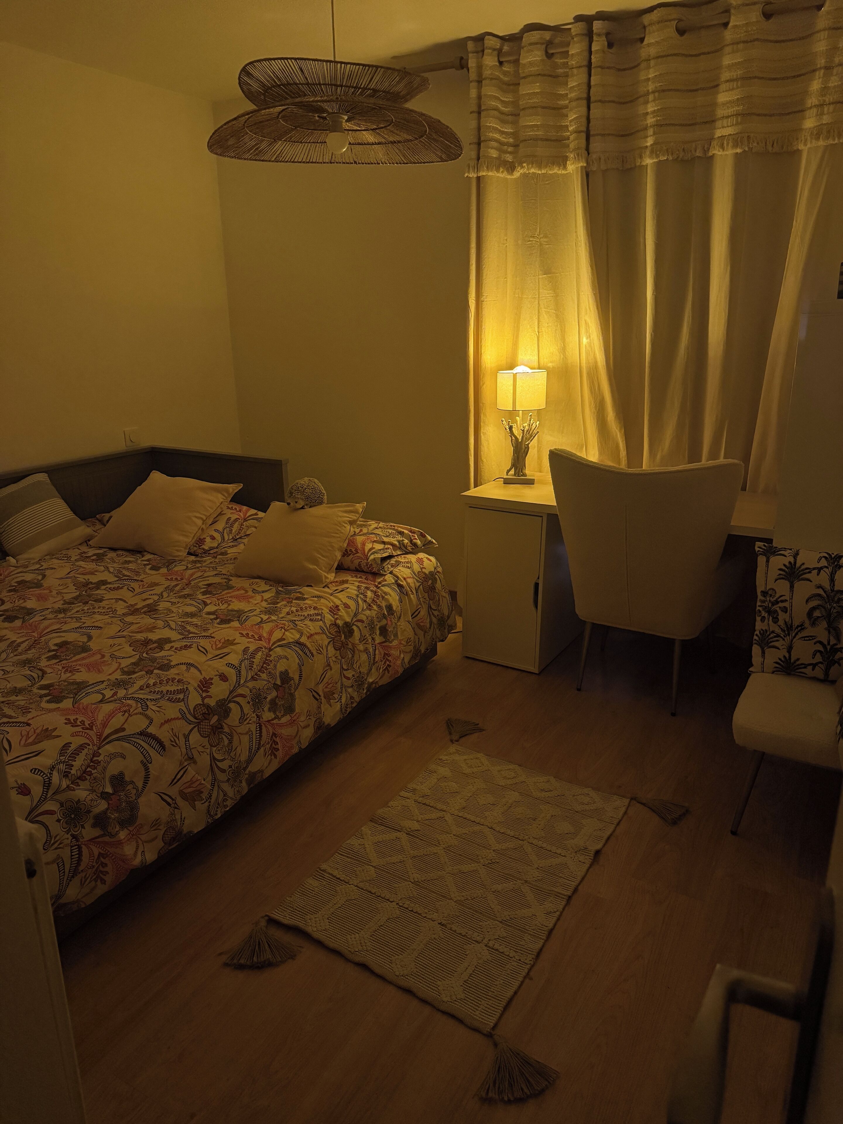 Ein Schlafzimmer mit einem Bett, einem Schreibtisch, einem Stuhl, einer Lampe und einer Pendelleuchte.
