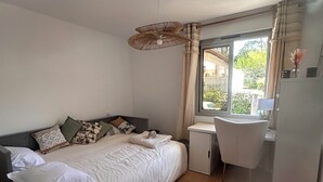 Un dormitorio con cama, mesita de noche, escritorio, silla y ventana con cortinas.