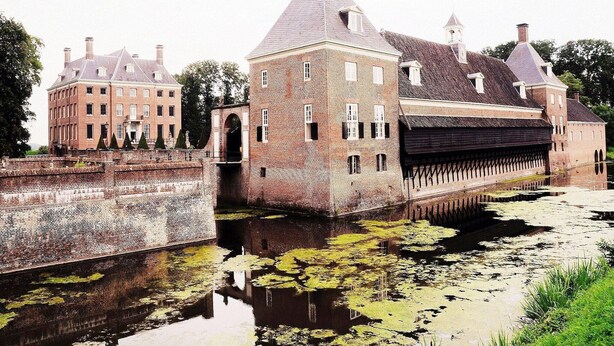 A historic building with a prominent tower and a moat with lily pads.