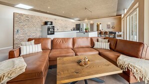 Een moderne woonkamer met een bruine leren hoekbank, een houten salontafel en een keuken op de achtergrond.