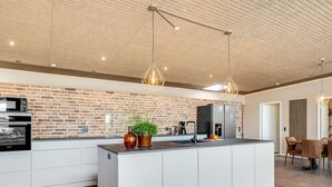 Een moderne keuken met een tegelachtergrond van baksteen, witte kasten en hanglampen.