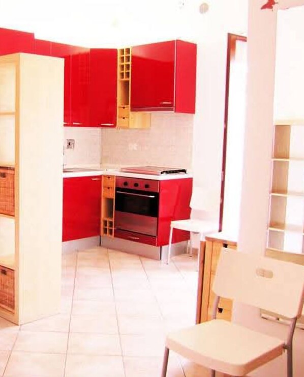 A compact kitchen with red cabinets, a stove, and a white chair. - The I Due Mari studio apartment is a charming open-concept space. (Lecce)