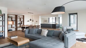 Una sala moderna con un sofá modular gris, una estantería de madera y un comedor con mesa y sillas.