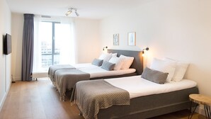Habitación de hotel con dos camas, televisión de pantalla plana, ventana grande con cortinas y una obra de arte en la pared.