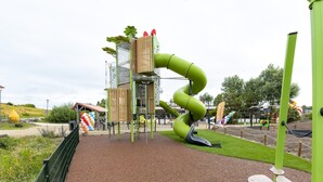 Un'area giochi con uno scivolo a spirale verde, strutture di arrampicata e un recinto.