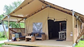 Une tente dotée d’une terrasse en bois, d’un espace salon et d’un petit coin cuisine.
