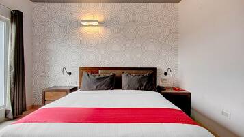 A hotel room with a bed, a nightstand, a lamp, and a wall with a circular pattern.