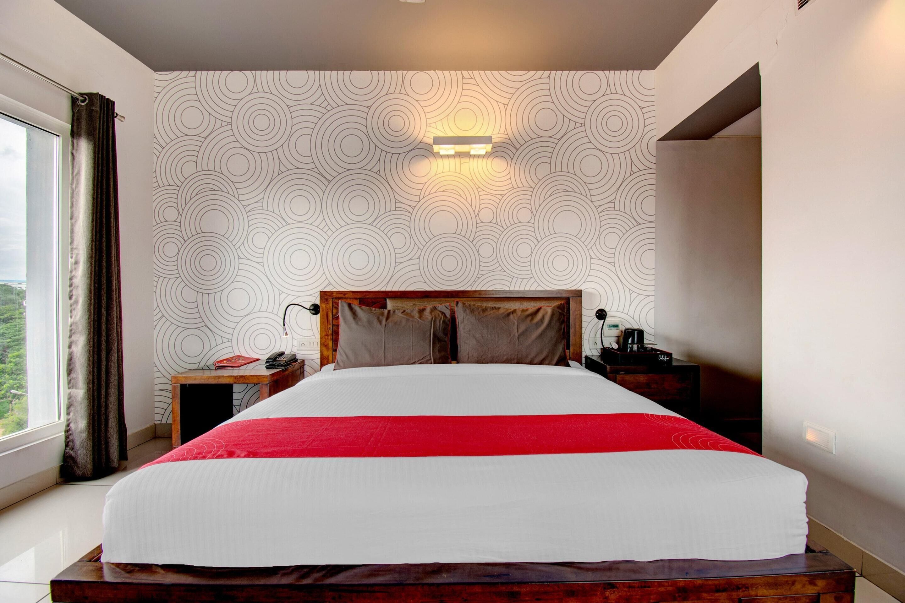A hotel room with a large bed, a nightstand, a lamp, and a view of the outdoors.