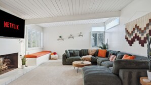 A modern living room with a sectional sofa, a flat-screen TV, and a fireplace. - La Jolla Oasis | 4BR Luxury | Hot Tub | Close to Beach | Sleeps 12 (San Diego)