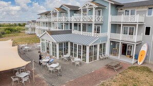 Un hotel frente a la playa con varios balcones, mobiliario exterior y una tabla de surf a la vista.