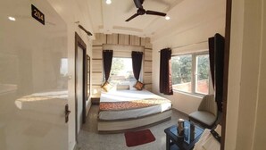 A bedroom with a bed, a ceiling fan, a window, and a door. - RUDRA GANGA HOTEL (Varanasi)